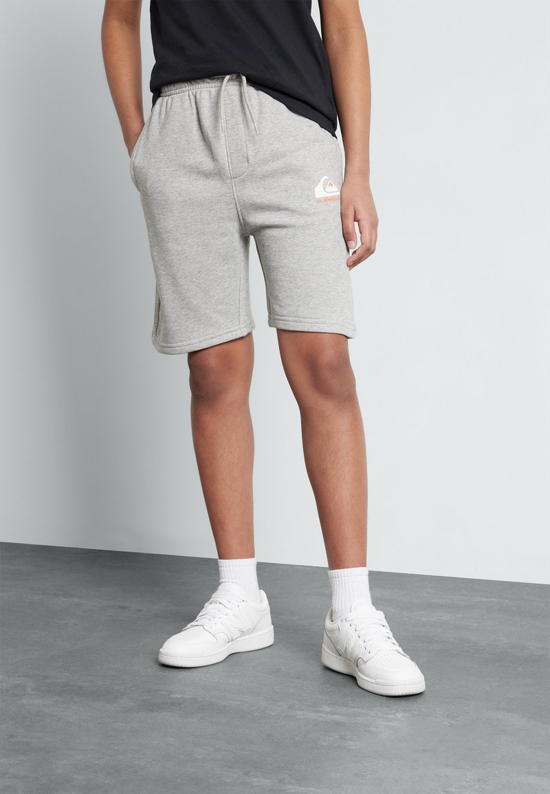 Grå bomullsshorts med elastisk liv, sidelommer og en liten logo foran. Hvite sneakers og ankelsokker fullfører utseendet.