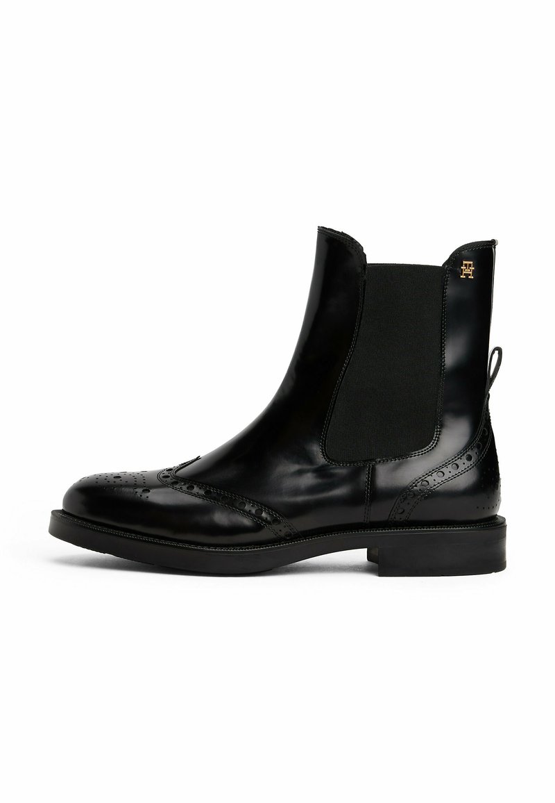 Des bottines Chelsea en cuir noir présentent une finition brillante, des panneaux latéraux élastiques, des détails en brogue sur le bout et une semelle en caoutchouc noir.
