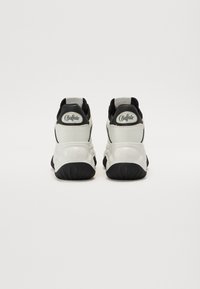 Weiße und schwarze Sneakers mit einer klobigen Sohle, aus Mesh- und Leder-Materialien, gepolstertem Kragen und "Buffalo"-Markierung an der Ferse.