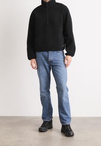Pullover nero in pile con zip a quarto, tessuto strutturato, vestibilità comoda. Abbinato a jeans azzurri a gamba dritta e sneakers nere.