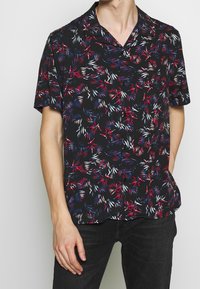 Kurzärmeliges Hemd aus leichtem Stoff mit schwarzem Hintergrund und bunten Blattmustern in Rot, Weiß und Blau.