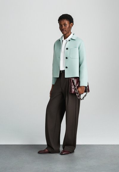 Minta zelena skrajšana jakna z črnimi gumbi, nošena preko bele srajce. Rjave široke hlače in burgundski quiltani ročno torbici s verigo.