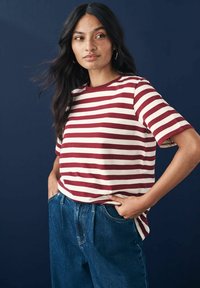 Rot- und cremefarbener gestreifter T-Shirt mit kurzen Ärmeln, rundem Ausschnitt und lockerer Passform, kombiniert mit hochgeschnittenen blauen Jeans.