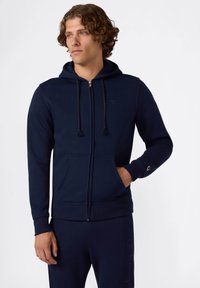 Felpa con zip di colore blu navy realizzata in tessuto misto cotone, caratterizzata da cordini regolabili, due tasche frontali e dettagli con logo sul petto e sulla manica.