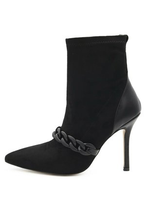 Stivale alla caviglia nero con punta affilata, realizzato in suede e pelle. Presenta un dettaglio a catena sul collo del piede e un tacco a spillo.