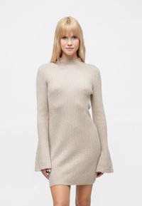 Μπεζ πλεκτό φόρεμα με ριγέ υφή, ψηλό λαιμόκοψη και μακριά φαρδιά μανίκια, με διακριτό σχέδιο και εφαρμοστή γραμμή.