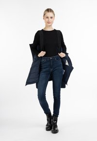 Giubbotto imbottito blu navy con zip, indossato sopra un top nero a maniche lunghe, abbinato a jeans skinny blu e stivali neri alla caviglia.