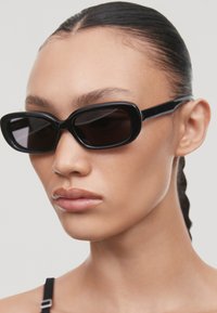 Ochelari de soare rectangulare negri cu rame groase și lentile închise la culoare. Designul are o finisare netedă și o estetică minimalistă.