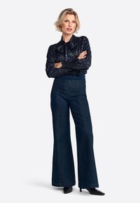Navy blouse with textured floral design, tied collar; paired with wide-leg dark denim pants and pointed black heels.