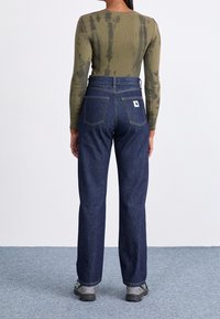 Cotton long-sleeve shirt in olive with a tie-dye pattern, paired with dark blue straight-leg jeans featuring back pockets and a logo patch.