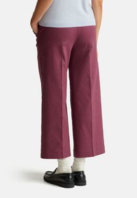 Bordowe spodnie o szerokich nogawkach z wysokim stanem, z bocznymi kieszeniami i gładką fakturą. W zestawieniu z czarnymi butami i białymi skarpetkami.