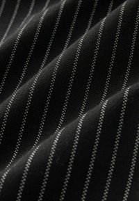Schwarzer Stoff mit schmalen weißen Nadelstreifen, glatte Textur und sichtbaren Nähten. Sanft gefaltet angeordnet, um das Muster hervorzuheben.