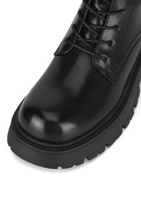 Czarny skórzany botek za kostkę o gładkim wykończeniu, zaokrąglonym nosku i solidnej, teksturowanej gumowej podeszwie. Posiada sznurowanie oraz wzmocnione przeszycia.