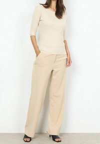 Beige geribbelde gebreide top met ellebooglange mouwen, gecombineerd met beige wijde broekspijpen en zwarte sandalen met hak. Eenvoudig en strak ontwerp.