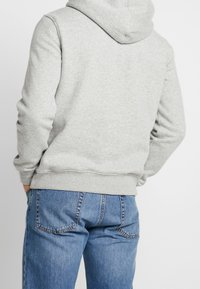 Sudadera gris con capucha, que presenta puños y dobladillo acanalados. Combinada con unos vaqueros de denim azul, que exhiben un ajuste relajado y detalles en el bolsillo trasero.