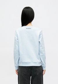 Sweatshirt azul claro feito de tecido suave, apresentando um decote redondo ribado e punhos, com o logótipo "KARL LAGERFELD" em preto na parte de trás do pescoço.