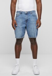 Shorts en denim bleu clair avec une coupe décontractée, un design à cinq poches et un ourlet effiloché. Portés avec un débardeur blanc et des baskets blanches.