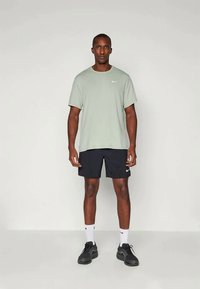 Vaaleanvihreä lyhythihainen T-paita, jossa on valkoinen Nike-logo, mustien shortsien ja mustien urheilukenkien kanssa, seisovan hahmon päällä.