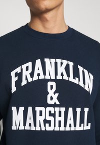 Felpa blu navy in cotone, con grande scritta bianca "FRANKLIN & MARSHALL" sul petto in un carattere audace e sportivo.