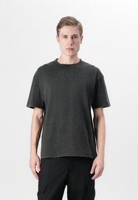 T-shirt en coton noir avec une coupe décontractée, texture usée, décolleté rond et manches courtes. Détail de logo subtil sur la poitrine.