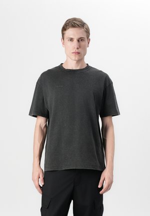 Schwarzes Baumwoll-T-Shirt mit lockerer Passform, distressed Struktur, rundem Halsausschnitt und kurzen Ärmeln. Subtiler Logo-Detail im Brustbereich.