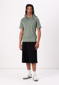 Tricou din bumbac de culoare verde deschis, cu mâneci scurte, croială lejeră. Asortat cu pantaloni scurți negri și pantofi albi cu accente negre. Design simplu.