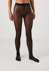 Collants noirs translucides avec une texture lisse, dotés d'une ceinture large et d'une couture au centre. Design pied et matériau léger.