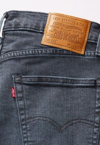 Ciemnoszare dżinsy z denimu z brązową skórzaną metką z napisem "Levi Strauss & Co." oraz czerwoną etykietą na szwie lewego kieszonki.