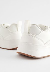 Hvide sneakers lavet af syntetisk materiale med en tekstureret overflade, der har en afrundet tå, polstret krave og en gummisål.