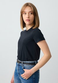 T-shirt nera a maniche corte con scollatura rotonda, realizzata in tessuto liscio. Indossata con jeans blu a vita alta e una cintura nera.
