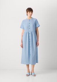 Abito azzurro chiaro a maniche corte con pois neri, chiusura a bottoni frontale, arricciature in vita e gonna fluida. Abbinato a sandali azzurri chiari.
