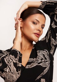 Czarna bluzka z wzorem falistych złotych linii, długimi bufiastymi rękawami z marszczonymi mankietami oraz głębokim dekoltem w kształcie litery V.