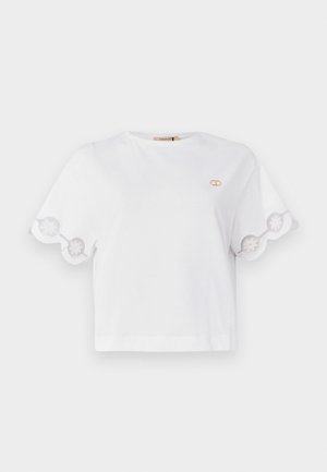 White cropped t-shirt made of cotton with scalloped embroidered sleeves and a small gold logo accent on the chest. Smooth texture.