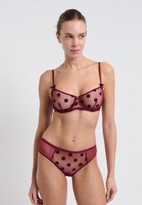 Bordowy zestaw biustonosza i fig z przezroczystego materiału siateczkowego z welurowymi kropkami, z wsparciem na drutach i regulowanymi ramiączkami. Proste akcenty w postaci kokardek.