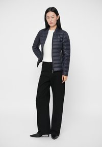 Navy puffer jacket with a quilted design and stand-up collar, paired with wide-leg black pants and pointed black shoes.
