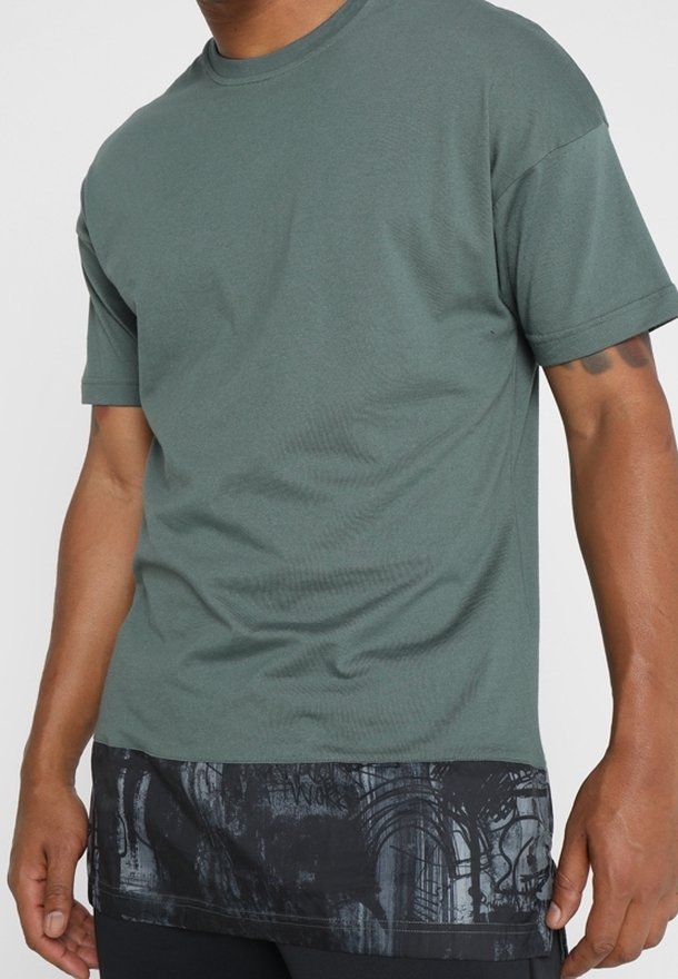 Green cotton T-shirt with a black patterned bottom. Short sleeves, round neckline, relaxed fit, and textured detailing on the hem.
