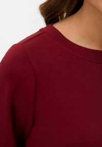 Camicia di cotone bordeaux con scollatura arrotondata e texture liscia, maniche corte e dettagli di cucitura sottili.