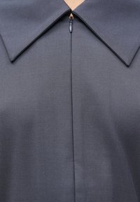 Tmavosivá košeľa s golierom a hladkou textúrou, so zipsom vpredu a širokým golierom. Tkanina má jemný lesk.