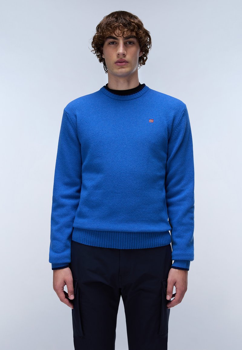 Blå stickad tröja med rund halsringning, ribbade ärmslut och nederkant; har en liten röd logotyp på bröstet. Tyget har en strukturerad yta.