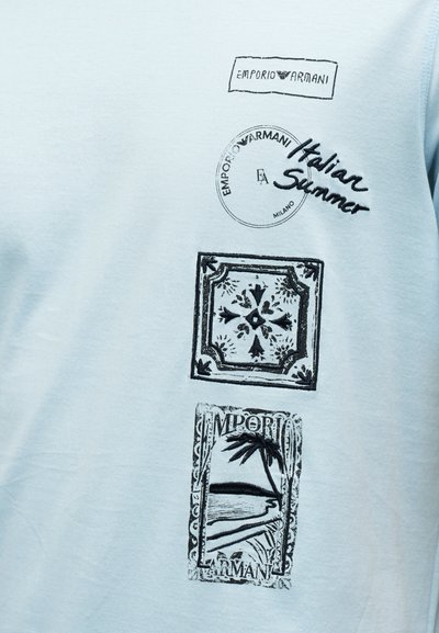 Ανοιχτό μπλε ύφασμα με μαύρο τυπωμένο κείμενο "Emporio Armani," "Italian Summer," διακοσμητικό τετράγωνο και σχέδια παραλίας με φοίνικες.