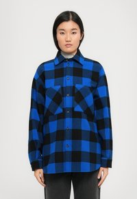 Camicia in flanella a quadri blu e nera con chiusura a bottoni, due tasche sul petto e colletto. Maniche lunghe e texture morbida.