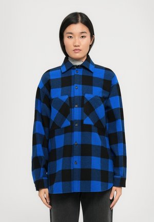 Camicia in flanella a quadri blu e nera con chiusura a bottoni, due tasche sul petto e colletto. Maniche lunghe e texture morbida.