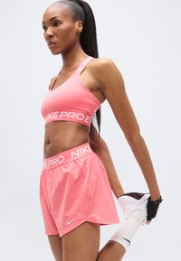 Den pink Nike Pro sports-bh og shorts har et logo-bånd, elastisk materiale og en tætsiddende pasform. Sokkerne er hvide; skoene er hvide og sorte.