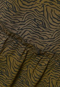 Tissu léger couleur vert olive avec un motif de rayures zèbre noires. Présente un ourlet à volants et des coutures visibles le long de la ceinture.