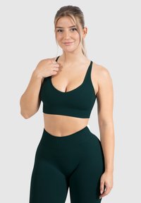 Sujetador deportivo de color verde oscuro con un escote en V profundo y tirantes anchos, combinado con leggings de cintura alta, todo en una tela suave y elástica.
