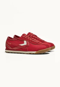 Röda canvas sneakers med en strukturerad ovandel, kontrasterande vit logotyp och detaljer, rund tå och en gummisul med ett zickzackmönster.