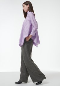 Lila shirt met een getextureerd voorpaneel, lange mouwen en een high-low zoom, gecombineerd met grijze brede broekspijpen en zwarte puntige schoenen.