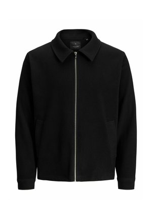 Veste zippée noire avec un col pointu, texture côtelée, poches latérales et une fermeture éclair argentée. Design simple, moderne et polyvalent.