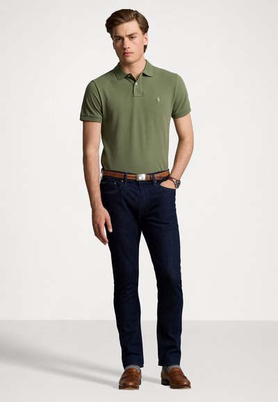 Tricou polo verde măsliniu cu mâneci scurte, asortat cu blugi negri din denim și pantofi din piele maro, cu un brâu maro și un ceas argintiu.