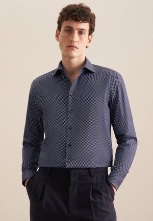 Marineblauw overhemd met knopen, bedekt met witte stippen, lange mouwen en een puntige kraag. De stof lijkt glad en heeft een getailleerde pasvorm.